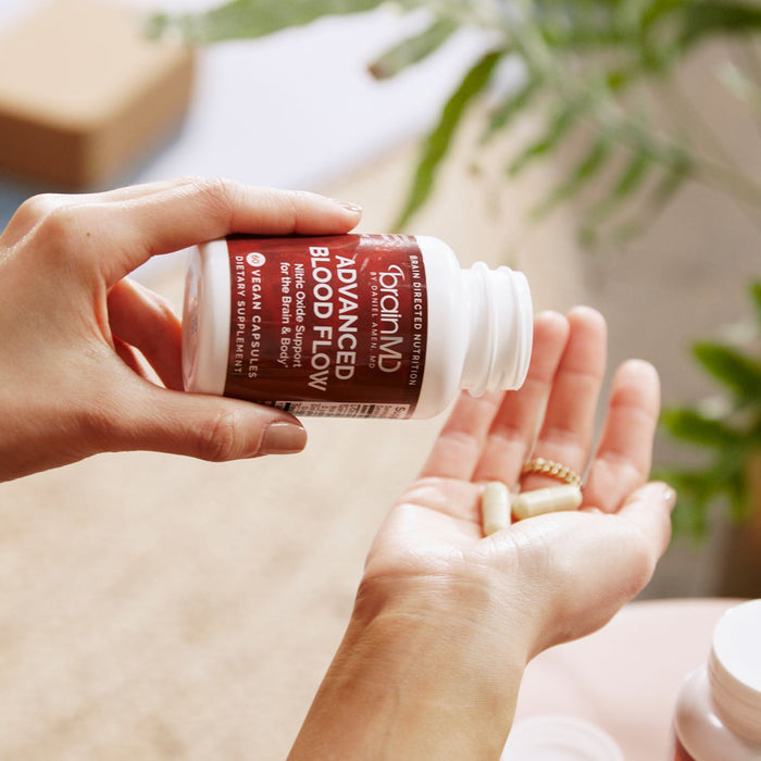BrainMD Advanced Blood Flow: person pouring capsules from a supplement bottle into hand with blurred out interior background
