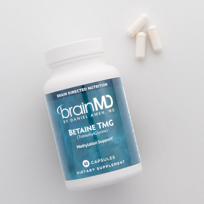 BrainMD Betaine TMG: blue supplement bottle with white capsules on a white surface