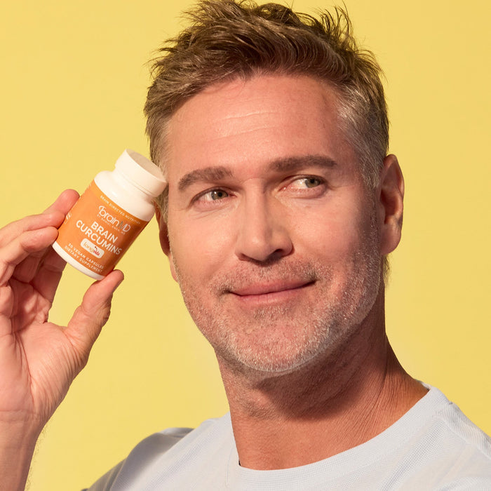 BrainMD Brain Curcumins: man holding orange supplement bottle to his temple in front of a yellow background