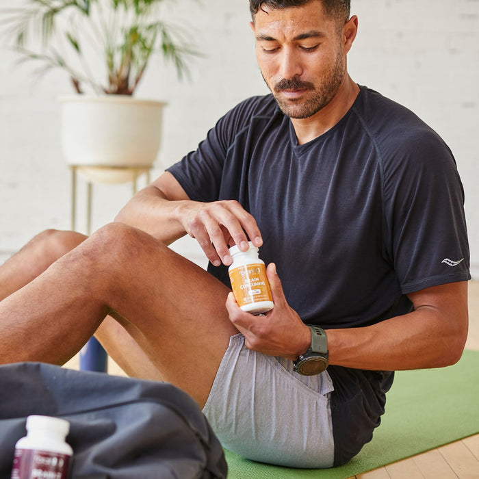 BrainMD Brain Curcumins: man holding orange supplement bottle in front of a blurred interior background