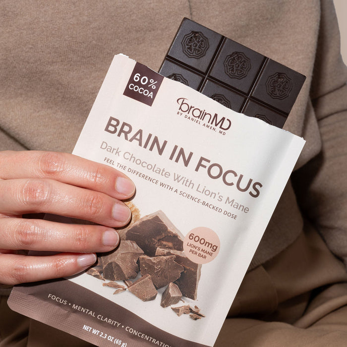 BrainMD Brain In Focus Chocolate: person holding large chocolate bar with chocolate squares visible above ripped package