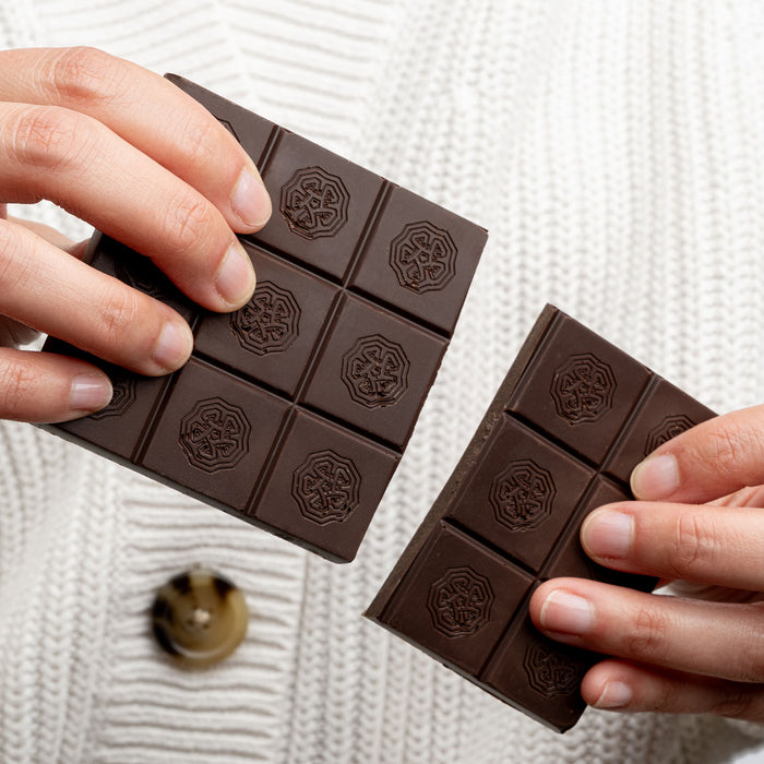 Person wearing a white sweater breaking apart a chocolate bar.