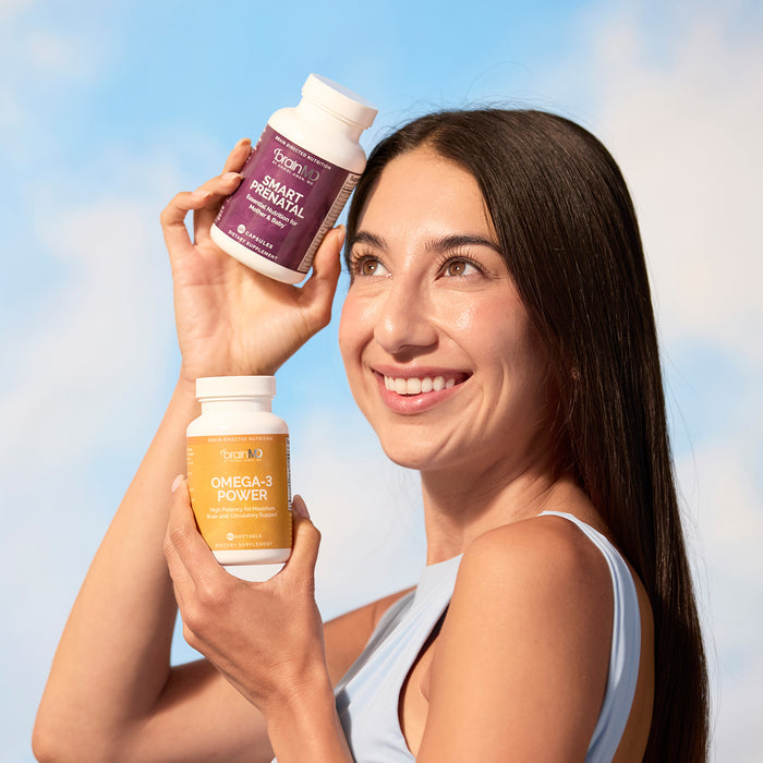 BrainMD Bundle Of Joy: woman holding purple and orange supplement bottles against a sky background