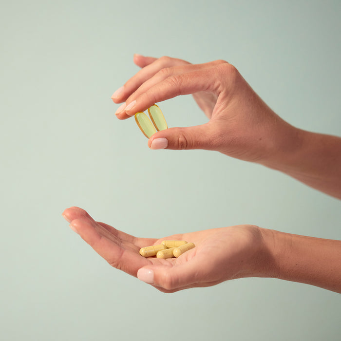 BrainMD Bundle Of Joy: woman holding softgels in one hand and capsules in the other against an off-white background