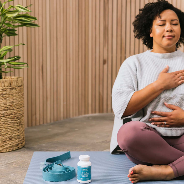 BrainMD Calm My Brain: woman doing breathing exercises with a blue supplement bottle on the mat next to her