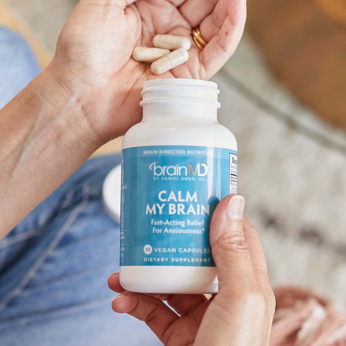 BrainMD Calm My Brain: person pouring capsules into hand from a blue supplement bottle