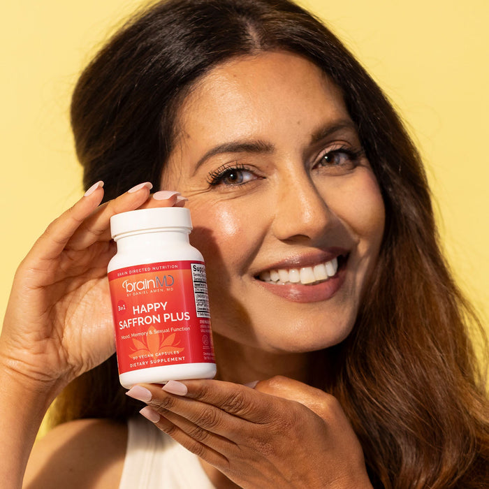 BrainMD Happy Saffron Plus: smiling woman holding a supplement bottle against a yellow background