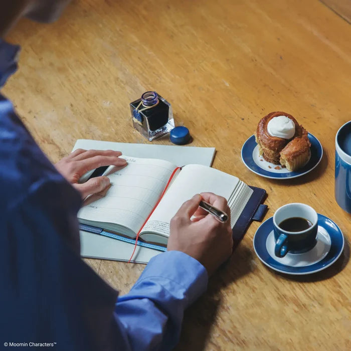 Hands writing in the open book at a café table, a cup of coffee nearby
