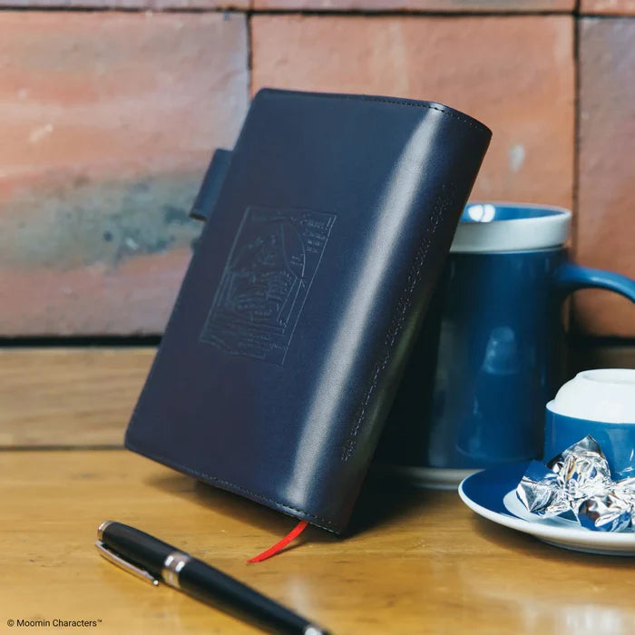 The cover standing upright on a wooden table next to a blue mug and saucer