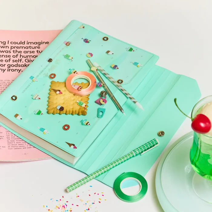 The cover open on a magazine with washi tape, a pen and a biscuit resting on it