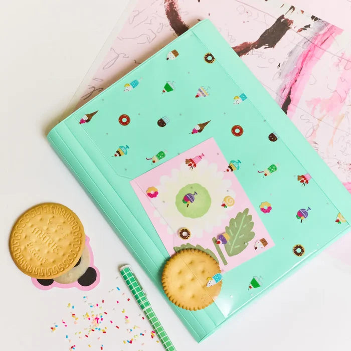 The closed cover on a pink card, biscuits and confetti scattered around it
