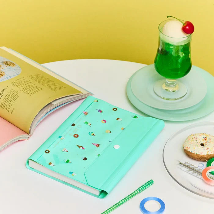 The cover on a white table beside an open book and a tall green cream soda