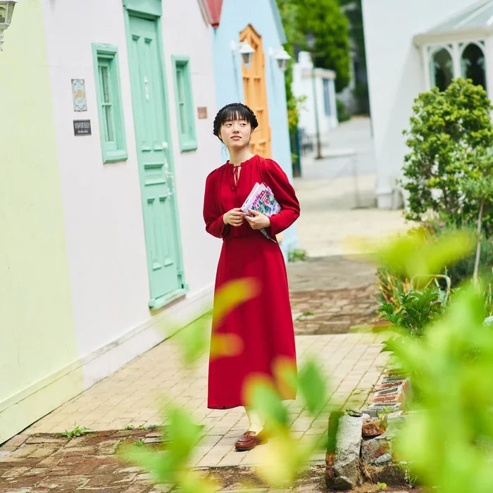 A woman in red on a pastel street, the cover held in her hands