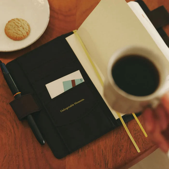 The cover open on a desk beside a cup of coffee and a biscuit