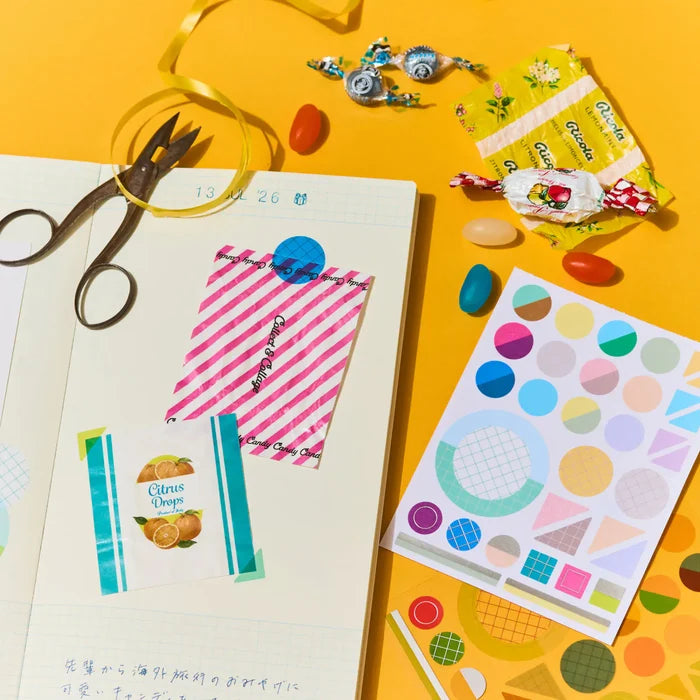 An overhead of a warm ochre desk: scissors, tape, sticker sheets and collected ephemera mid-arrangement