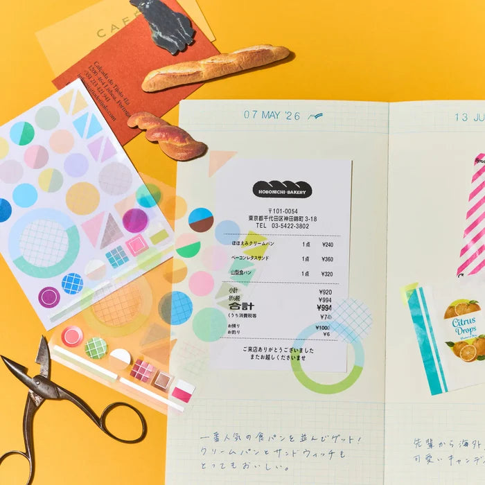 A hand pressing tape onto a journal page, sticker sheets and scissors laid out alongside