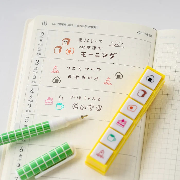 An open techo monthly page marked up with stamped icons, washi tape and a pen