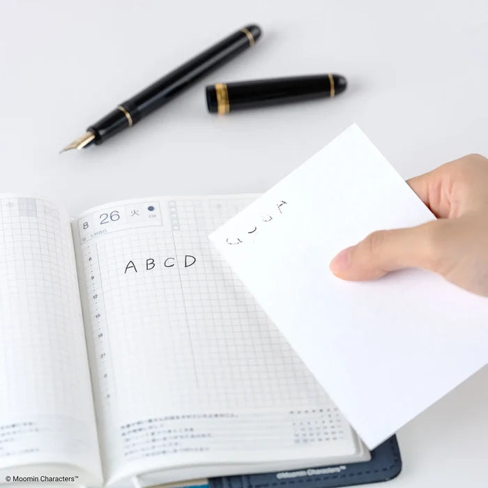 A hand laying a sheet down onto an open techo page, a fountain pen resting above