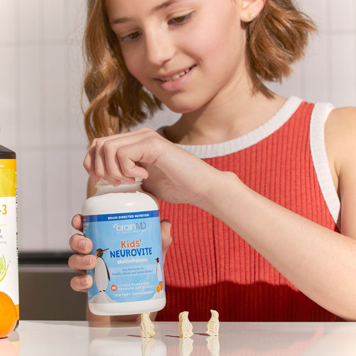 BrainMD Kids' NeuroVite Multivitamin Chewables: young girl opens blue supplement bottle, penguin-shaped vitamins on counter