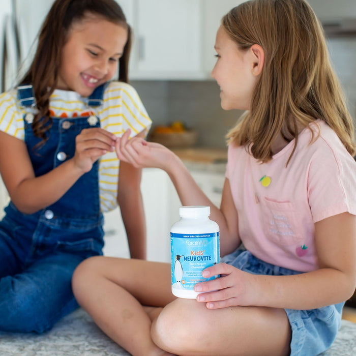 BrainMD Kids' NeuroVite Multivitamin Chewables: young girl holds blue supplement bottle, hands vitamin to friend