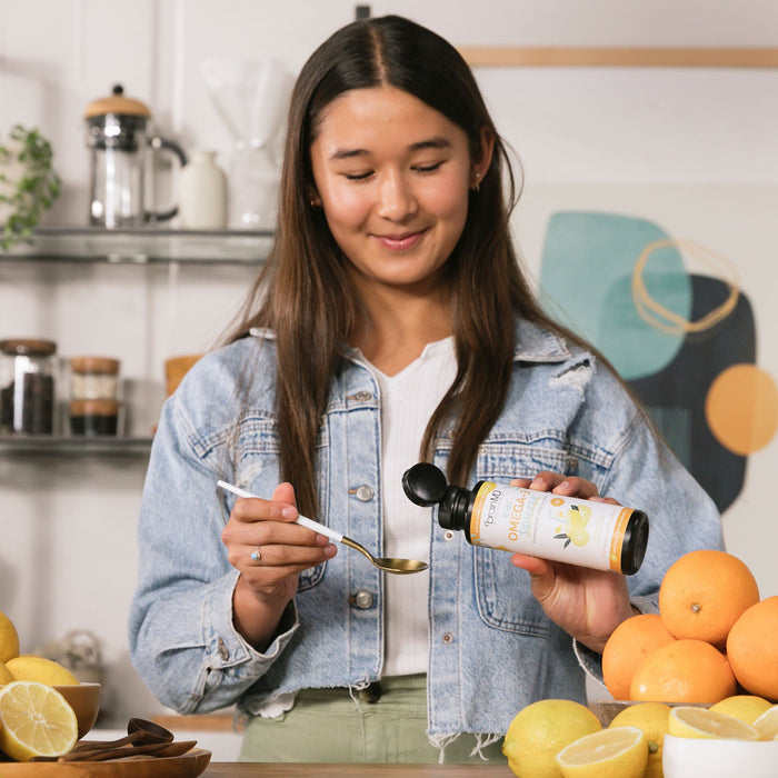 BrainMD Kids' Omega-3 Squeeze: woman in kitchen pouring liquid from a supplement bottle into a spoon
