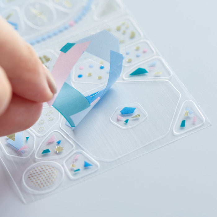 Hand peeling a HITOTOKI Coffret cosmetic film roll sticker onto paper.