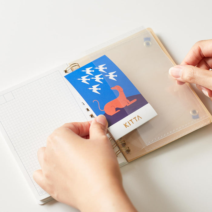 Hands opening a HITOTOKI passport size ring notebook and inserting a card.