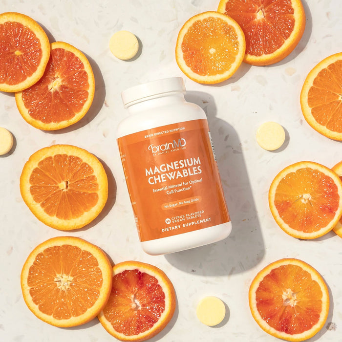 BrainMD Magnesium Chewables: orange supplement bottle on off-white surface surrounded by magnesium tablets and orange slices