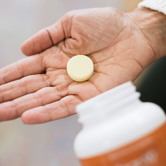 BrainMD Magnesium Chewables: magnesium tablet in person's hand, blurred orange supplement bottle in foreground