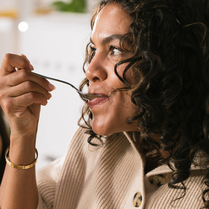 BrainMD Memory Bundle: woman sipping liquid vitamin C from a spoon, blurred interior background