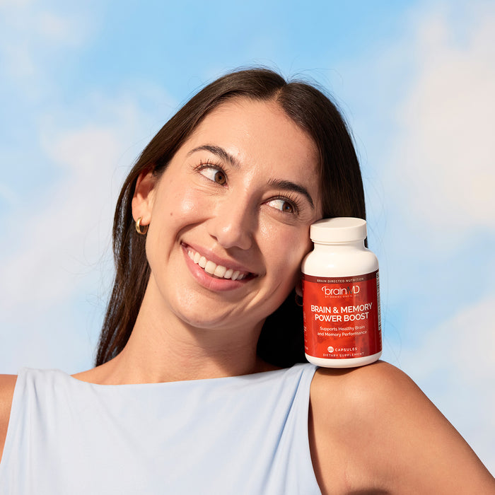 BrainMD Memory Bundle: woman balancing a red supplement bottle on her shoulder, blue sky background