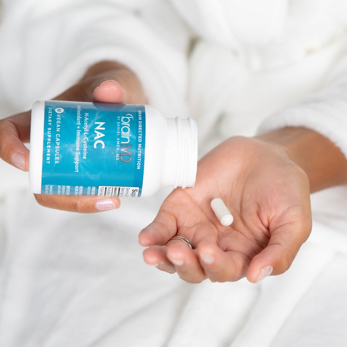 BrainMD NAC: person pouring a white capsule into their hand from a blue supplement bottle