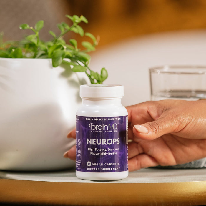 BrainMD Neuro-PS: person reaching for a purple supplement bottle, blurred interior background