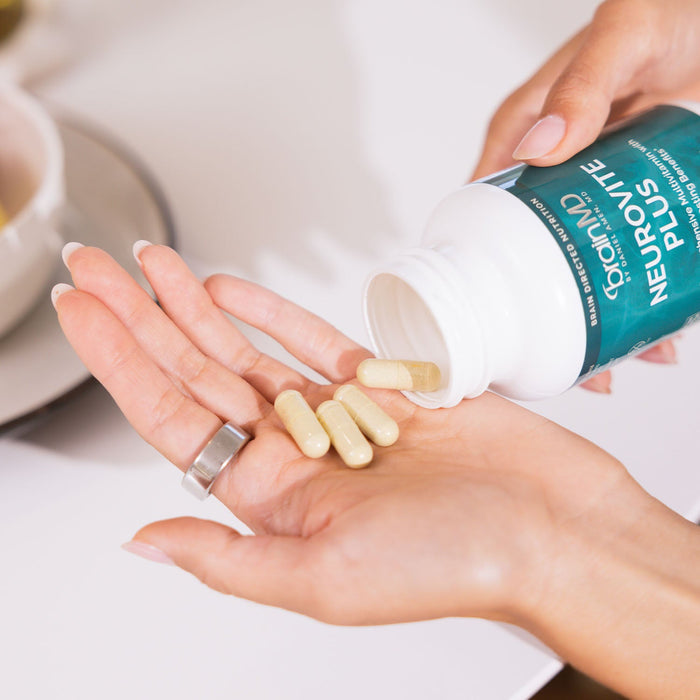 BrainMD NeuroVite Plus Multivitamin: woman pouring 4 capsules into her palm set against a blurry interior background