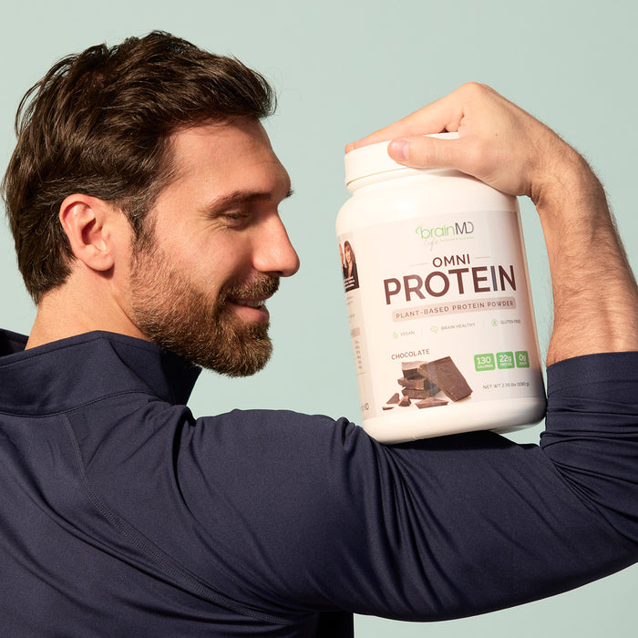 Smiling man holding a container of OMNI Protein powder against his flexed bicep.