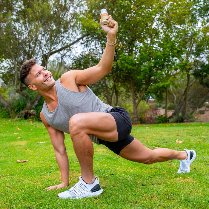 Man stretching in a park, holding up a bottle of Peak Energy.