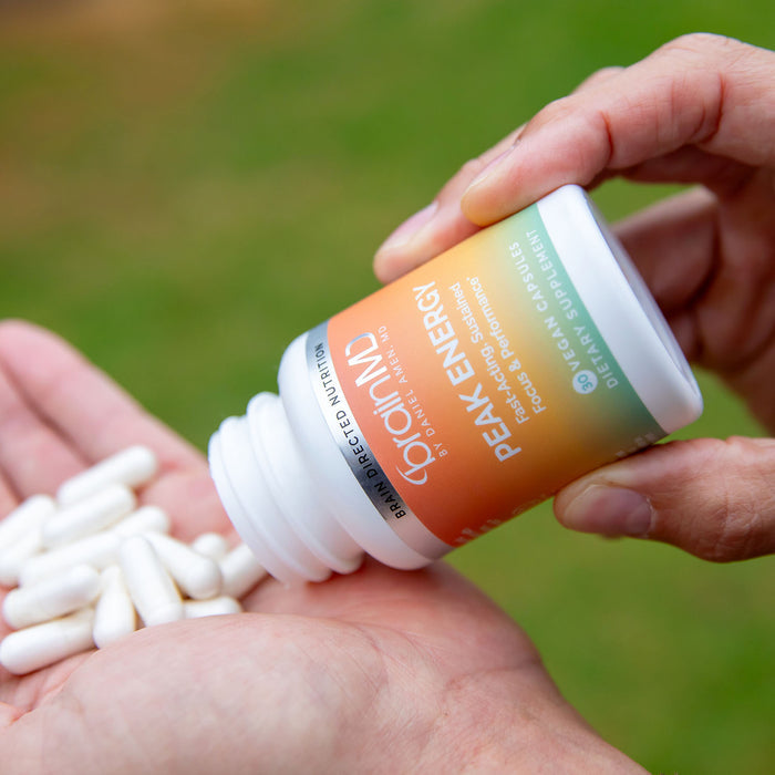 Hand pouring white capsules from a supplement bottle into a cupped palm.