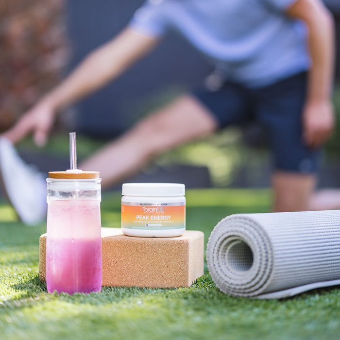 Blurred person stretching in the background, bottle w/ liquid, supplement container and mat in foreground.