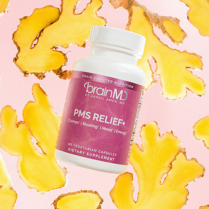 BrainMD PMS Relief+: pink supplement bottle against yellow root slices and a pink background