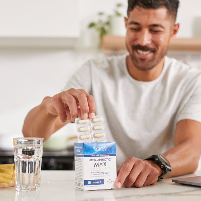 BrainMD ProBrainBiotics MAX: man pulling packaged capsules out of a blue & white supplement box with a blurred background