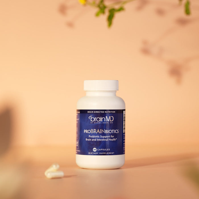 BrainMD ProBrainBiotics: blue supplement bottle and capsules sitting in front of a blurred peach-hued background