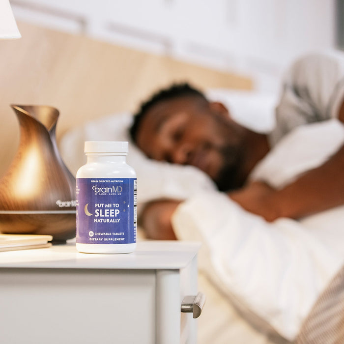 BrainMD Put Me To Sleep Naturally: purple supplement bottle on a nightstand with man sleeping in the background