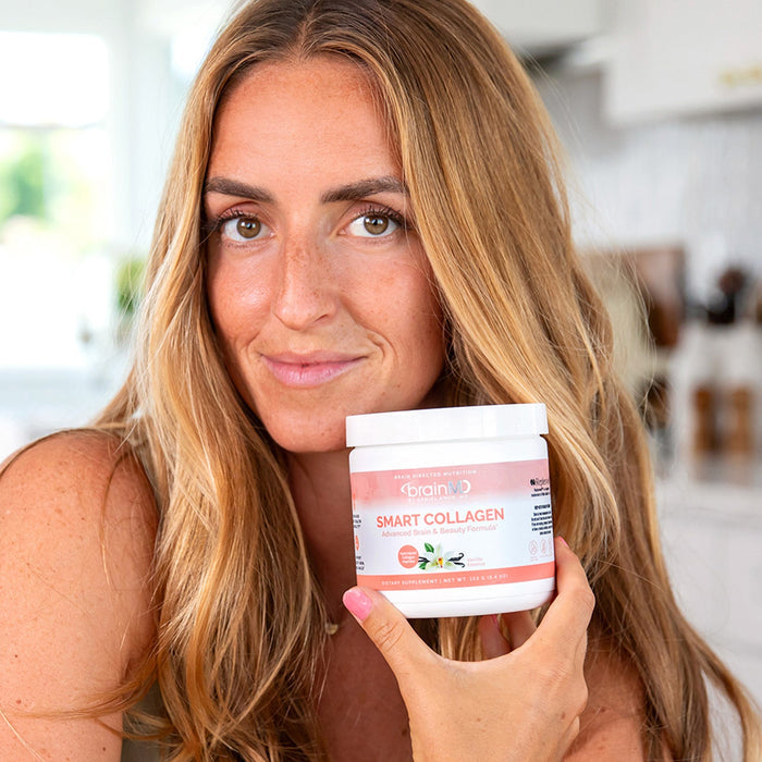 BrainMD Smart Collagen: woman holding a peach-hued supplement container in front of a blurred kitchen background
