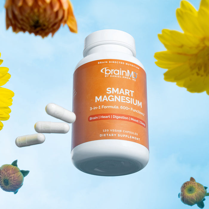 Low angle shot of orange supplement bottle, 3 white capsules and flowers against a powder blue background.