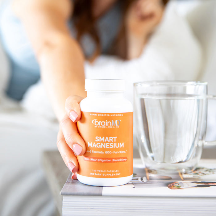 Woman's hand holding an orange supplement bottle next to a glass of water on a nightstand.