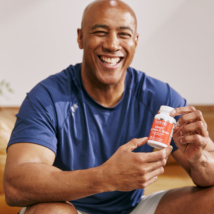 BrainMD Smart Metabolic Burn: smiling man holding red supplement bottle, blurred interior background