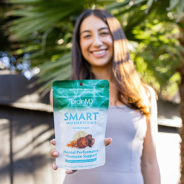 BrainMD Smart Mushrooms: smiling woman blurred in the background, holding a supplement bag toward the camera