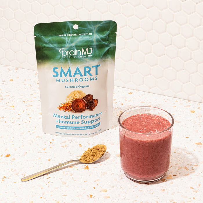 BrainMD Smart Mushrooms: supplement bag, spoonful of powder, and glass with smoothie in it, interior white background