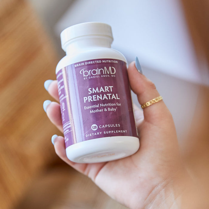 BrainMD Smart Prenatal: woman holding purple supplement bottle against a blurred interior background