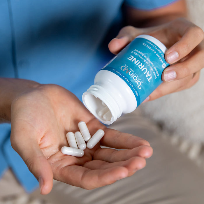 Person holding a bottle of Taurine supplements with capsules in their hand.
